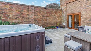 A backyard with a hot tub, outdoor seating, a brick wall, and a door leading to a covered area. - 2 Bed in Driffield (oc-79280) (Wold Newton)