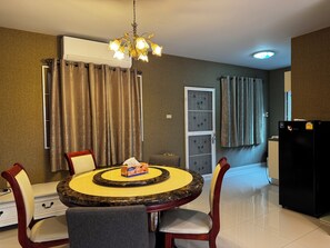 A dining area with a round table, chairs, a chandelier, an air conditioner, and a refrigerator. - Simple and Private Living Home near Suvarnabhumi Airport 23 min (บางโฉลง)
