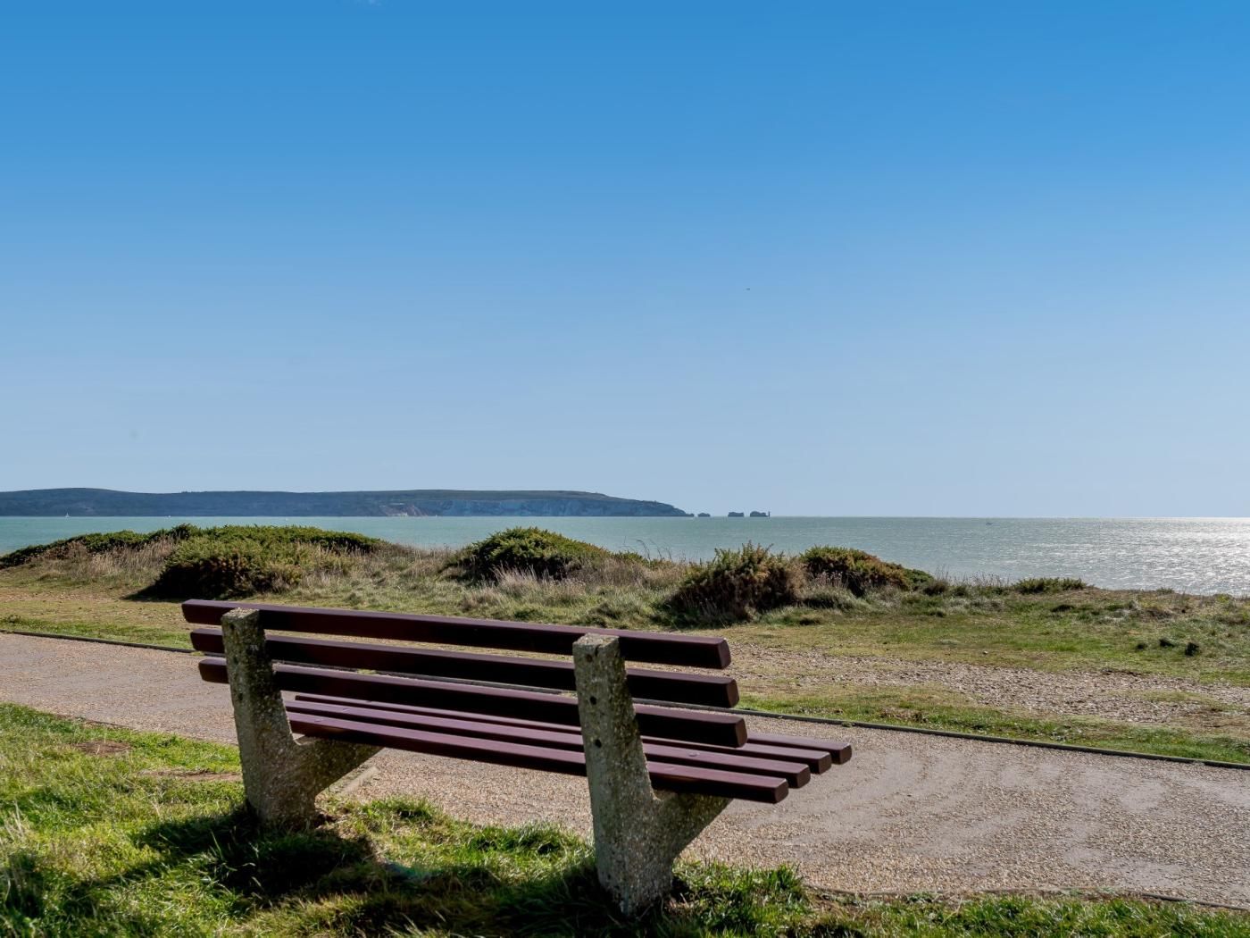 Un banc al costat d'un camí costaner amb vista despejada al mar i a paisatges llunyans.
