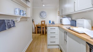 A compact kitchen with white cabinets, a wooden countertop, a clock, and a bread container. - 1 Bed in Lymington (oc-79332) (Milford on Sea)