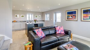 A modern living room with a black leather sofa, a coffee table, and a kitchen in the background. - 1 Bed in Harrogate (oc-79400) (Felliscliffe)