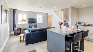 A modern kitchen with a built-in stove, a dining area with a black sofa, and a small island with bar stools. - 1 Bed in Harrogate (oc-79400) (Felliscliffe)