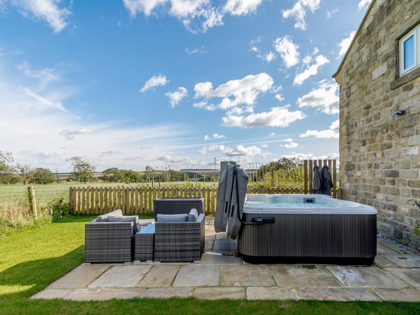 Un bain à remous avec une terrasse en bois, des sièges d’extérieur et un bâtiment en pierre en arrière-plan.