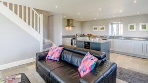 A modern kitchen with a central island, a dining area with a black leather sofa, and a staircase leading to another level. - 1 Bed in Harrogate (oc-79400) (Felliscliffe)