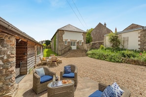 A stone cottage with a gravel patio, wicker furniture, and a small outdoor seating area.