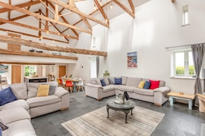 A spacious living area with a high ceiling, a dining area, and a view of the outdoors.