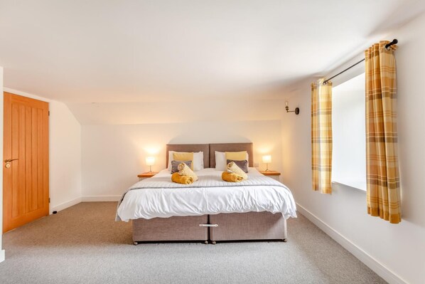 A bedroom with a bed, two bedside tables, a window with curtains, and a door.