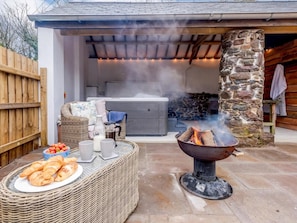 An outdoor patio with a stone fireplace, a wicker table with food and drinks, and a stone wall in the background.