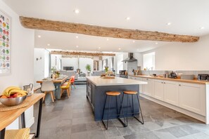 A modern kitchen with a central island, bar stools, and a dining area with a table and chairs. - 6 Bed in Petrockstow (oc-79407) (Petrockstow)