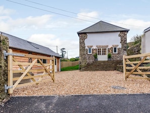 A stone building with a white door and windows, a gravel driveway, and wooden gates.