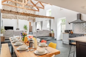 A spacious living area with a dining table set for a meal, a kitchen with modern appliances, and a stone wall.