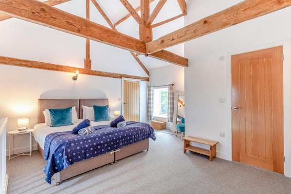 A bedroom with a large bed, wooden beams, a wooden door, and a window with curtains.
