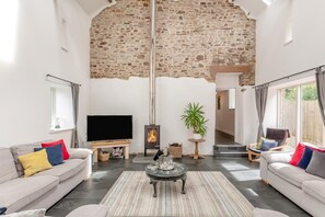 A living room with a stone wall, a fireplace, a television, and two sofas with cushions. - 6 Bed in Petrockstow (oc-79407) (Petrockstow)
