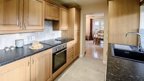 A kitchen with wooden cabinets, a black countertop, an oven, and a sink. - 2 Bed in Torrington (oc-79483) (Langtree)