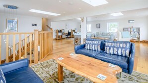 A spacious living area with a wooden staircase, a blue sofa, a wooden coffee table, and a bookshelf. - 4 Bed in Dunoon (oc-79529) (Ardentinny)