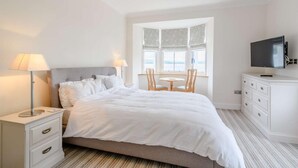A hotel room with a bed, bedside tables, a lamp, a TV, a window with a view, and a chair. - 4 Bed in Dunoon (oc-79529) (Ardentinny)