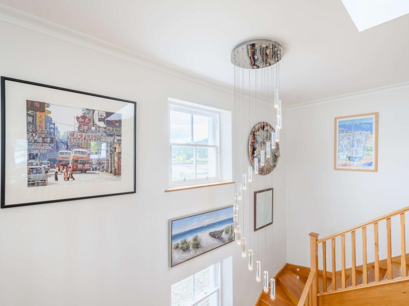 A staircase with wooden railings, a hanging light fixture, and framed artwork on the walls.