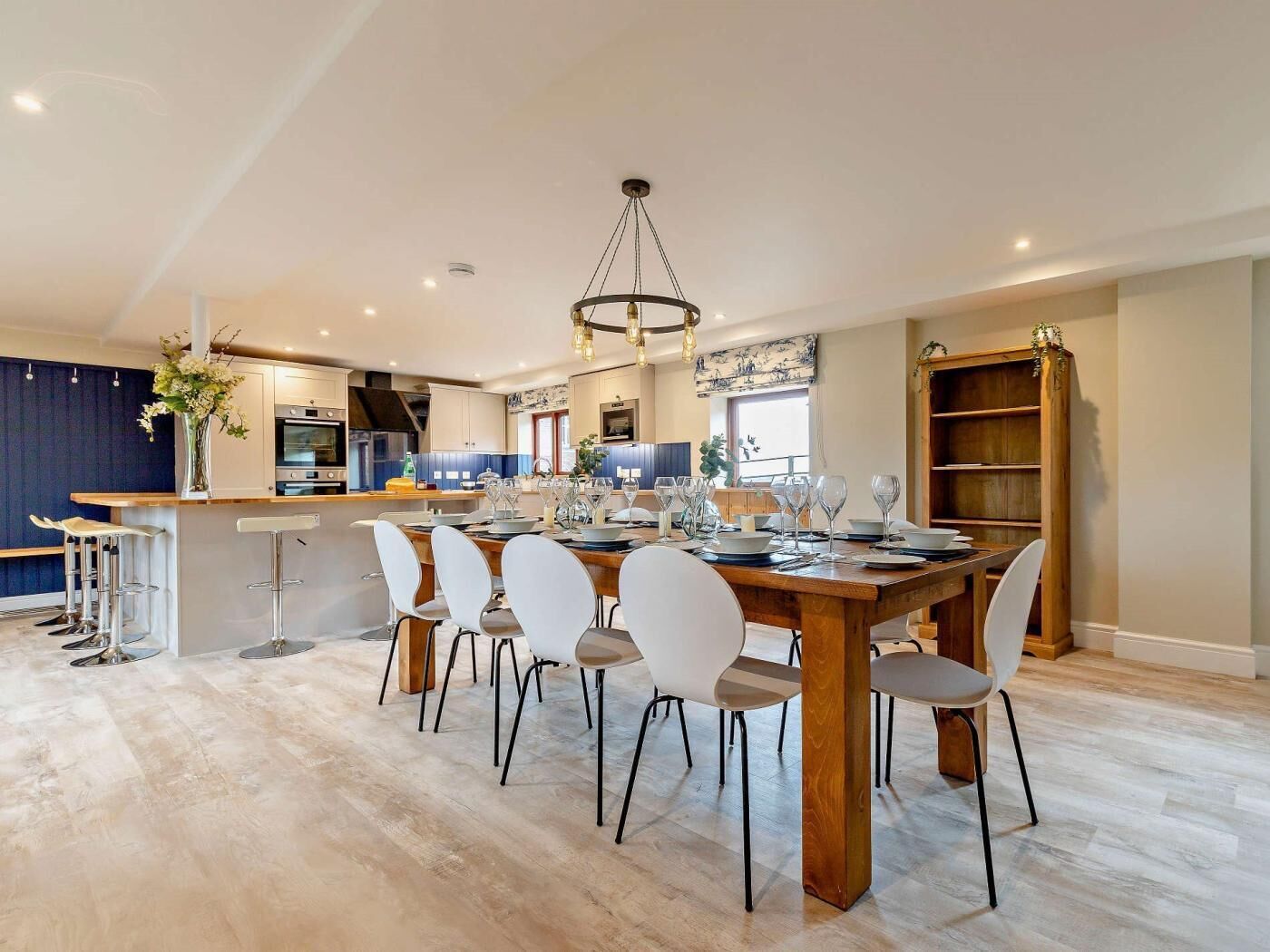 Cocina moderna con comedor, que incluye una mesa de madera, sillas blancas y una isla central con taburetes.