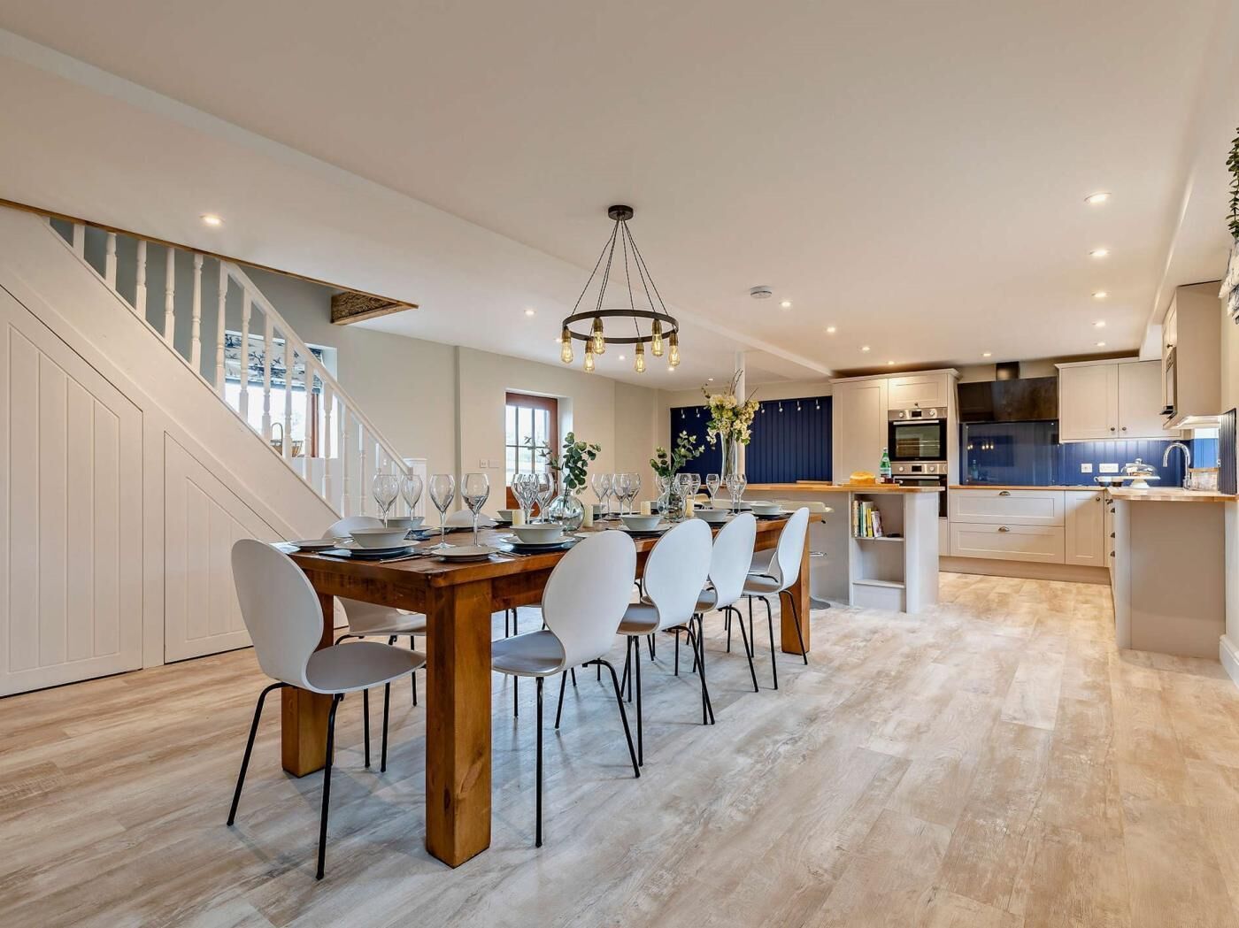 A modern kitchen with a central island, a dining area with a wooden table and chairs, and a staircase leading to an upper level.
