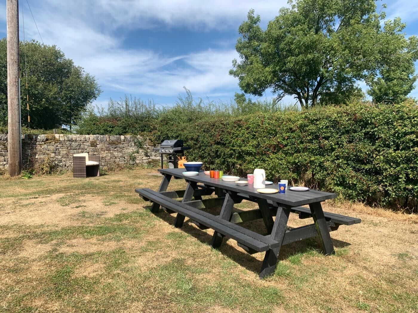 Un coin pique-nique aménagé à l’extérieur, avec une table, des chaises et un barbecue.