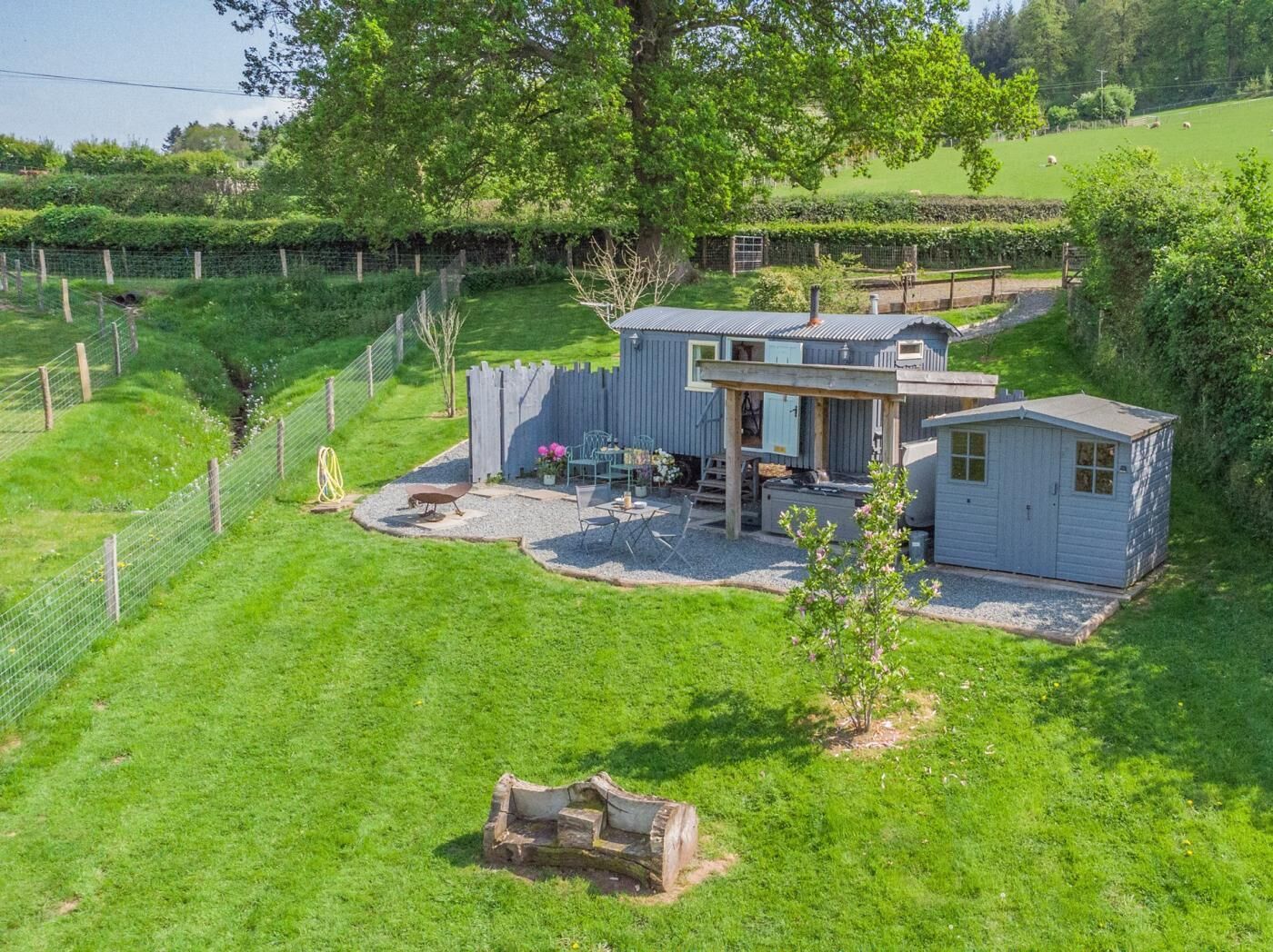 Un chalet rustique doté d’une terrasse, entouré d’une végétation luxuriante et d’une cour clôturée.