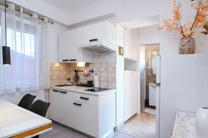 A modern kitchen with white cabinetry, a built-in stove, and a dining area with a table and chairs. - Villa Bazilika (Piran)