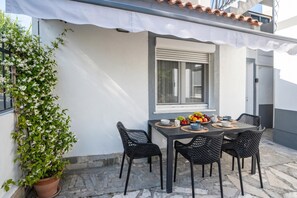 A patio with a table set for two, surrounded by chairs, a potted plant, and a window with blinds. - Villa Bazilika (Piran)