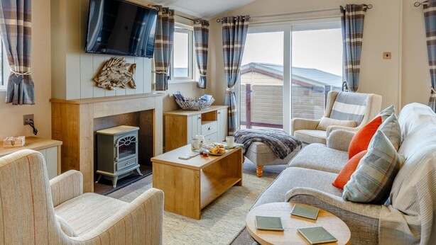 A cozy living room with a fireplace, comfortable seating, a flat-screen TV, and a large window with curtains. - 2 Bed in Brixham (oc-79989) (Brixham)
