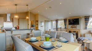 A modern kitchen with a central island, a dining area with a long table, and a living space with a fireplace. - 2 Bed in Brixham (oc-79989) (Brixham)