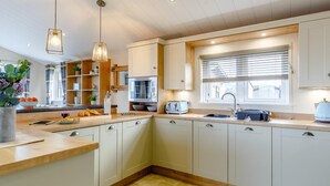 A modern kitchen with white cabinets, a built-in microwave, a toaster, and a window with blinds. - 2 Bed in Brixham (oc-79989) (Brixham)