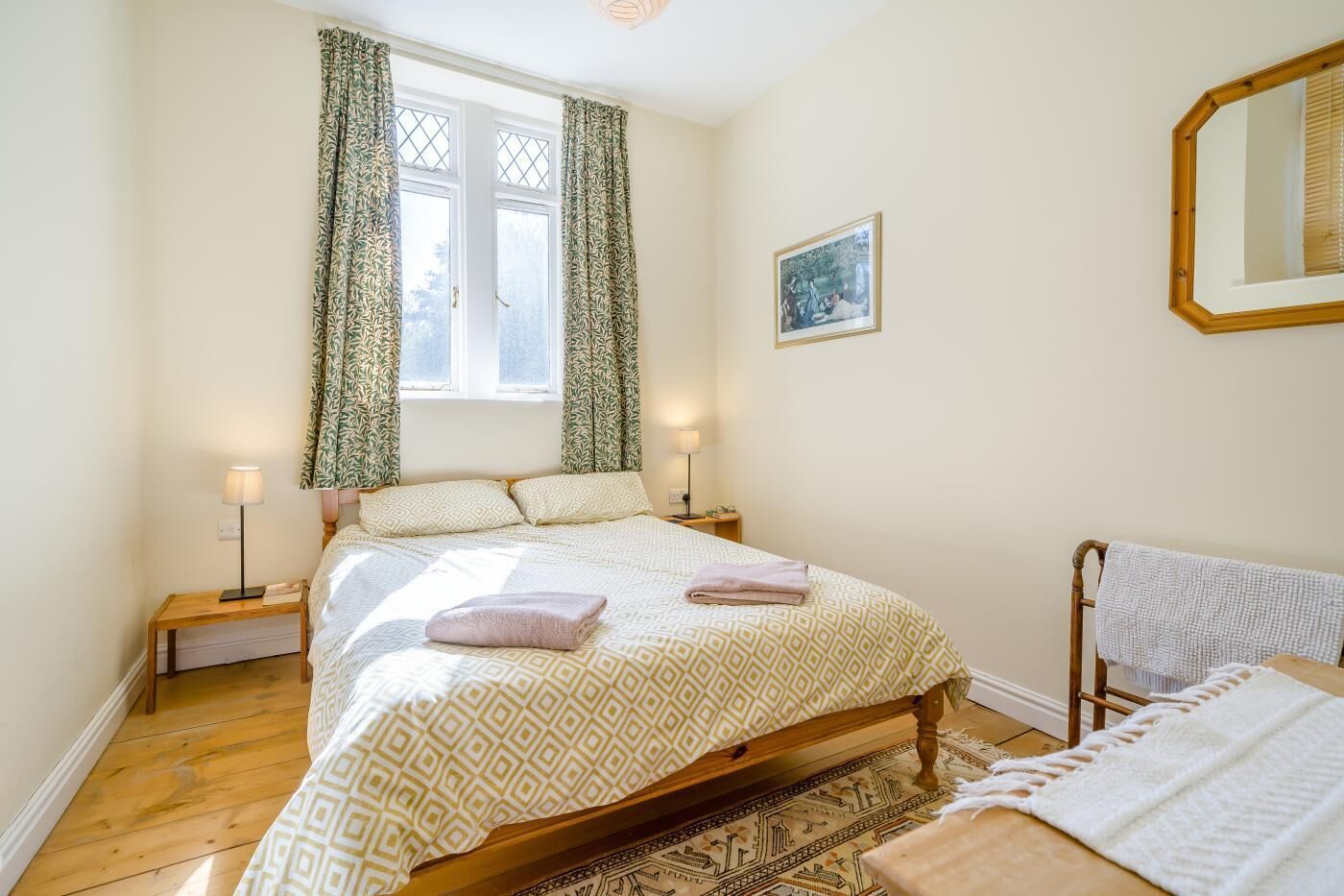 Une chambre à coucher comprenant un lit, deux tables de chevet, une fenêtre avec des rideaux, un miroir fixé au mur et un tapis.