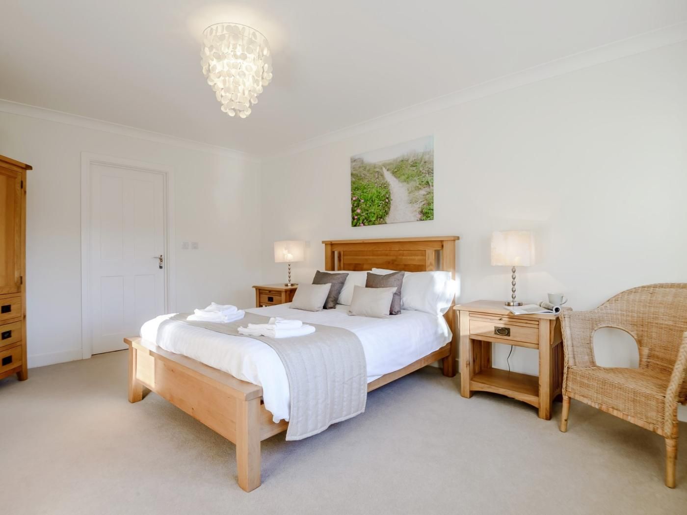 A bedroom with a wooden bed, bedside tables, a wicker chair, and a chandelier.