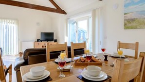 Un comedor con una mesa de madera, sillas y un televisor al fondo.