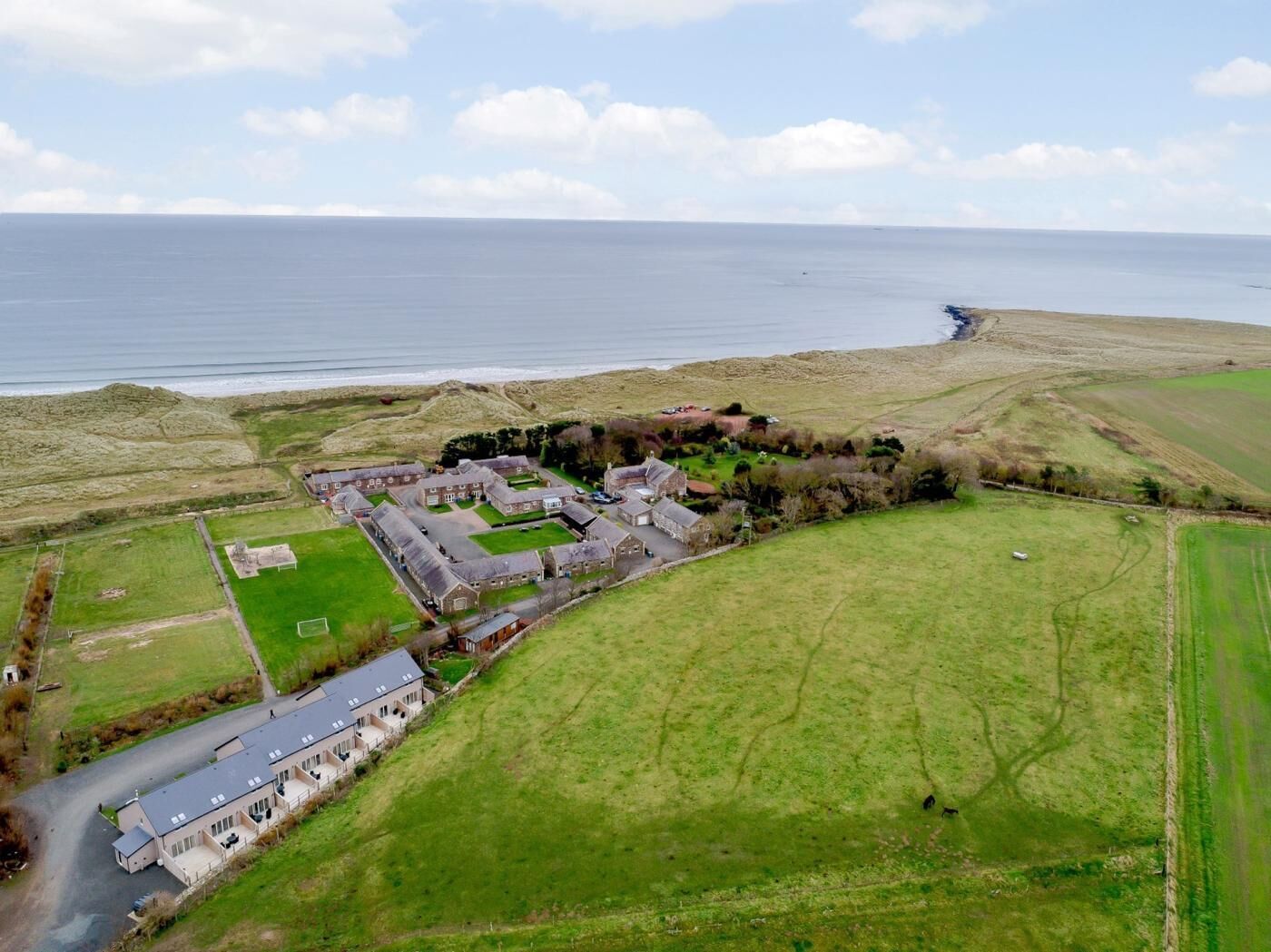 An aerial view of a coastal property with multiple buildings, including a large house with a long driveway and a smaller structure nearby.