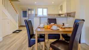 A dining area with a wooden table, black chairs, a kitchen in the background, and a staircase. - 2 Bed in Alnwick (oc-80488) (Newton-by-the-Sea)
