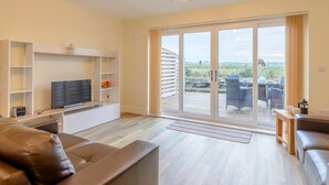 A modern living room with a TV, sofa, and a sliding glass door leading to an outdoor patio. - 2 Bed in Alnwick (oc-80488) (Newton-by-the-Sea)
