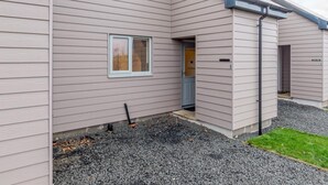 A two-story building with a grey siding exterior, a small window, and a door leading to a covered entrance. - 2 Bed in Alnwick (oc-80488) (Newton-by-the-Sea)