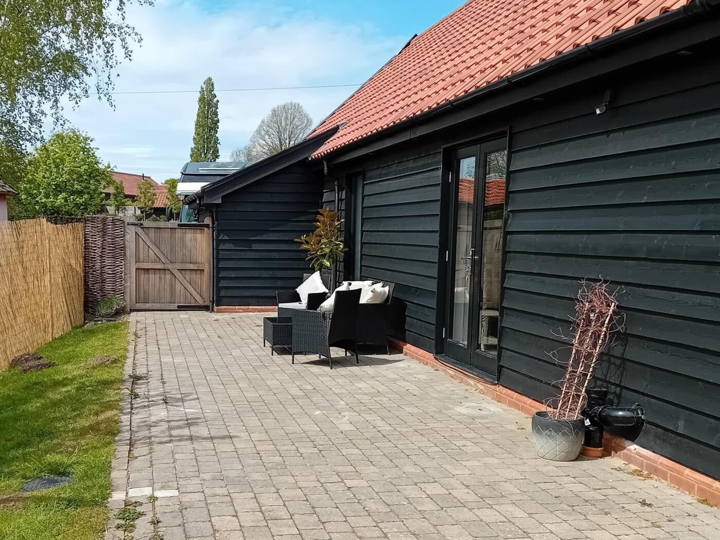 A black building with a red roof, a paved patio with outdoor furniture, and a wooden fence.