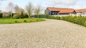 Een grindpad leidt naar een huis met een rood dak, omgeven door een verzorgd gazon en heggen.