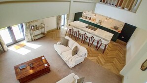 Een ruime woonkamer met een bank, een salontafel en een keuken met barkrukken.