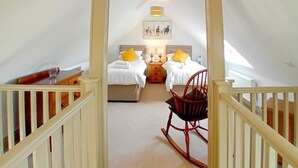 Een slaapkamer met twee bedden, een schommelstoel en een gang naar een andere kamer.