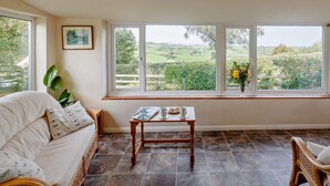 A room with a large window, a wooden table, a sofa, and a plant. - 2 Bed in Abergele (oc-80629) (Gwytherin)
