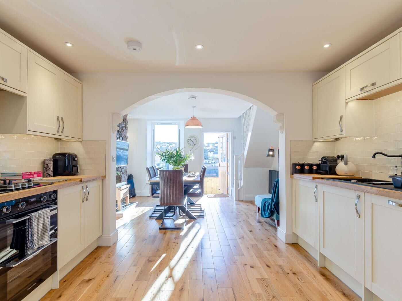 A modern kitchen with white cabinets, a dining area with a table and chairs, and a view through an archway to a balcony.
