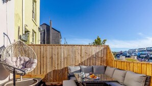 Eine Dachterrasse mit einer Rattan-Couch, einem Hängestuhl und einem Tisch mit einer Schüssel Essen.