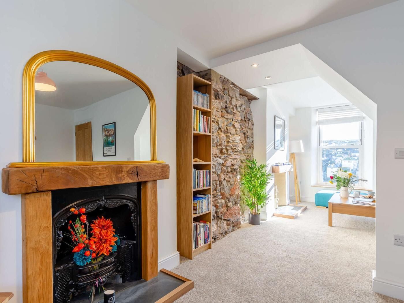 Ein Wohnzimmer mit Kamin, Bücherregalen, einer Steinwand und Blick durch ein Fenster.