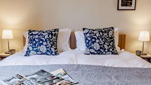 A neatly made bed with floral pillows, a magazine, and two bedside lamps. - 3 Bed in Chepstow (oc-81047) (Shirenewton)