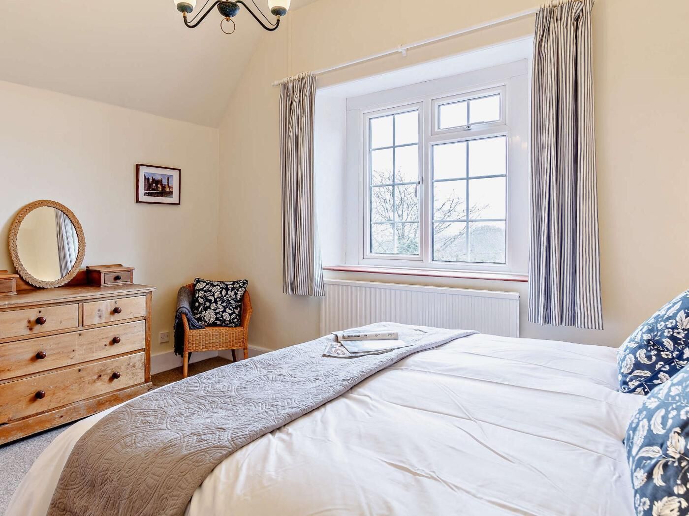 A bedroom with a bed, dresser, chair, window, and curtains.