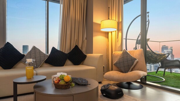 A modern hotel room with a sofa, armchair, and a table with fruit and a drink. - Spacious 3.5BR Burj LED View High Floor  (Dubai)