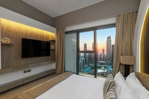 A modern hotel room with a large bed, a flat-screen TV mounted on the wall, and a cityscape view through large windows. - Spacious 3.5BR Burj LED View High Floor  (Dubai)