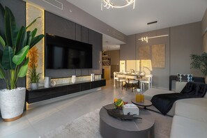 A modern living room with a flat-screen TV, a dining area with a table and chairs, and a kitchen in the background. - Spacious 3.5BR Burj LED View High Floor  (Dubai)